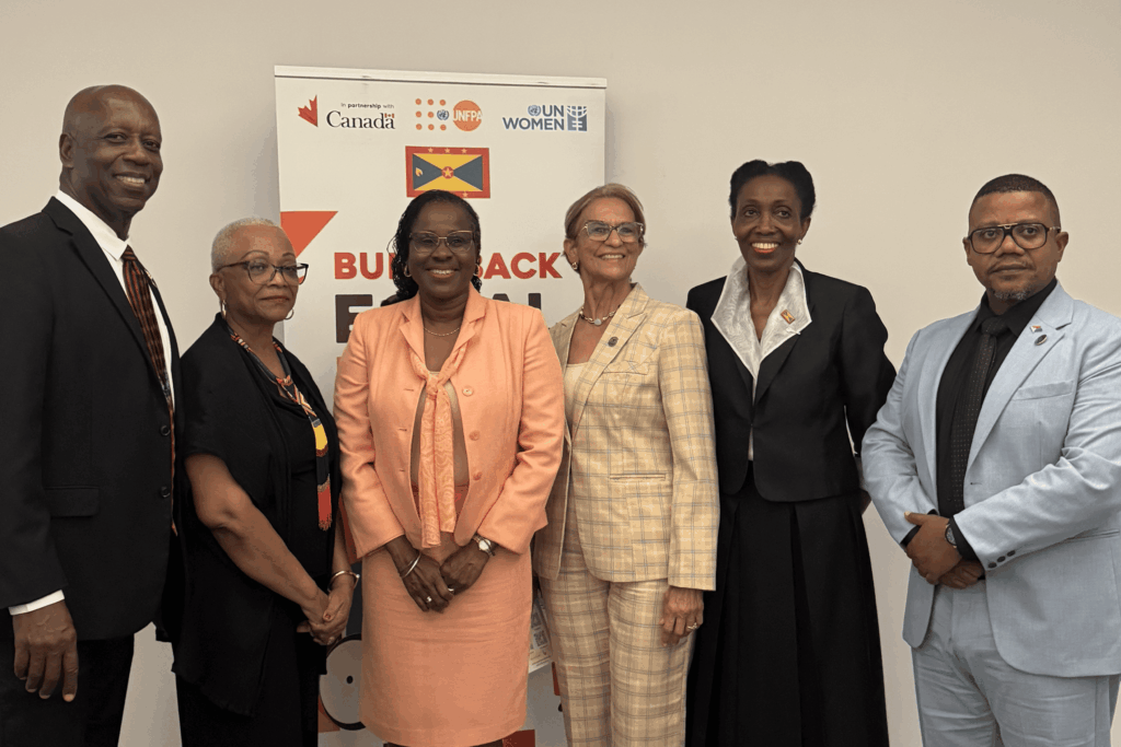 Six professionals in business attire pose together for a group photo at a formal event, with a logo banner in the background.