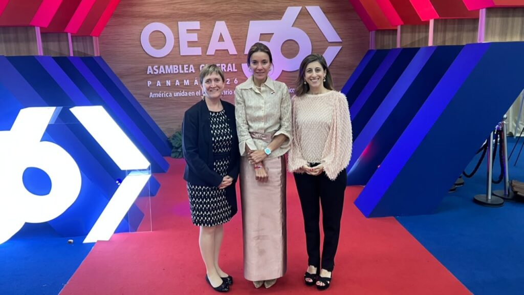 Three women pose on a red carpet at a formal event, with a bold geometric stage backdrop and large white sculpture (66) behind them.