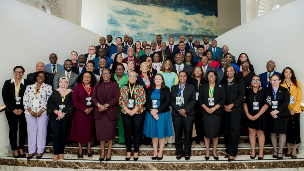Large diverse group of professionals in suits and dresses pose on marble stairs in a bright atrium, wearing event badges.
