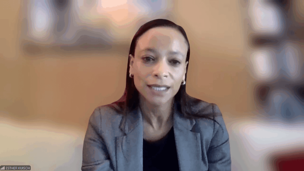 Esther Kuisch speaks during a video conference, wearing a gray blazer with a blurred background.