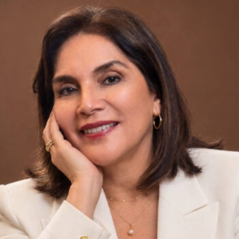 Professional headshot of a smiling woman with dark hair in a white blazer, her hand resting on her cheek.