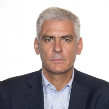 Formal portrait of a middle-aged man with short gray hair, wearing a navy blazer and light blue shirt, looking straight ahead.